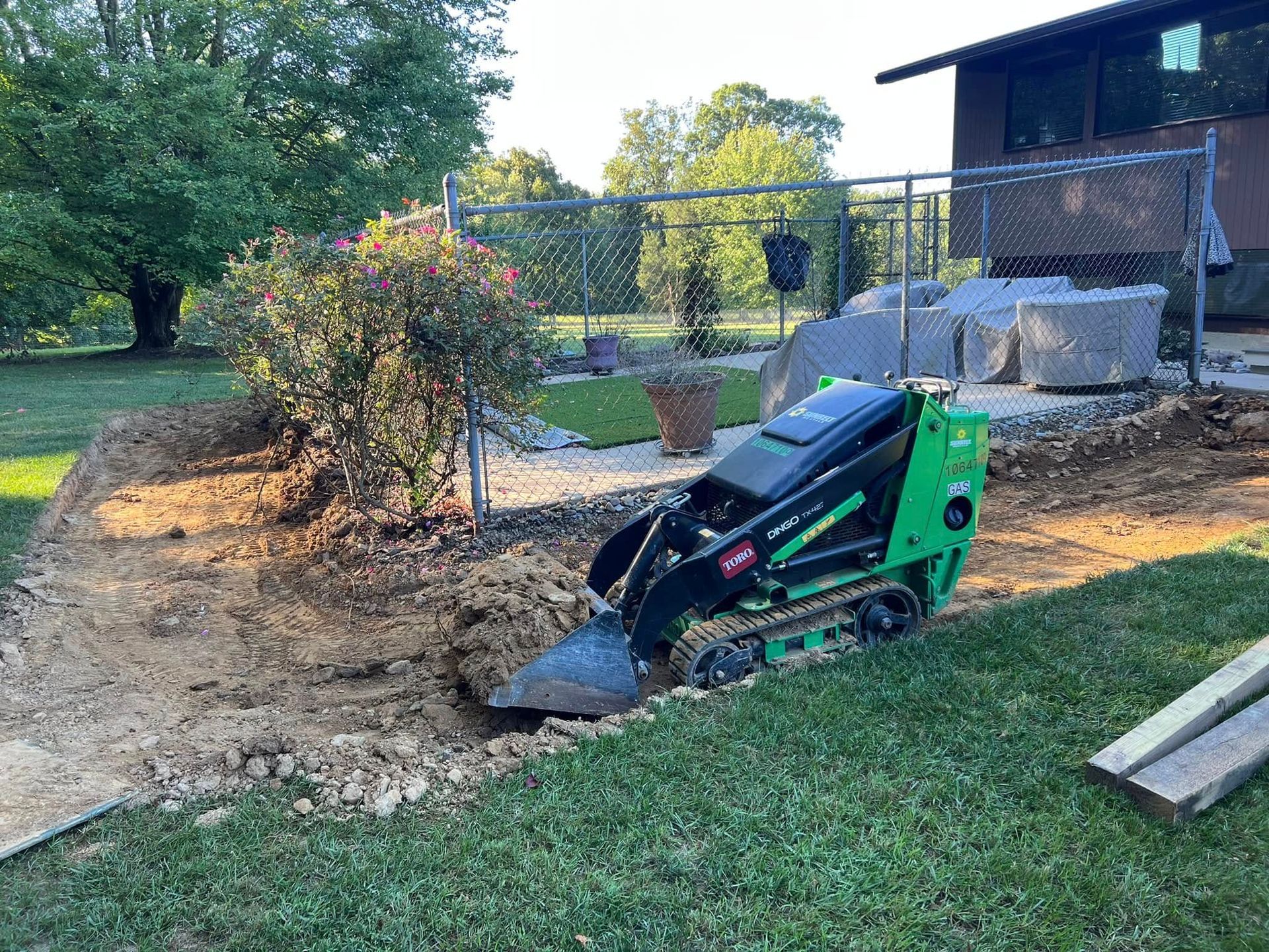 A green and black machine is digging a hole in the ground in a yard.