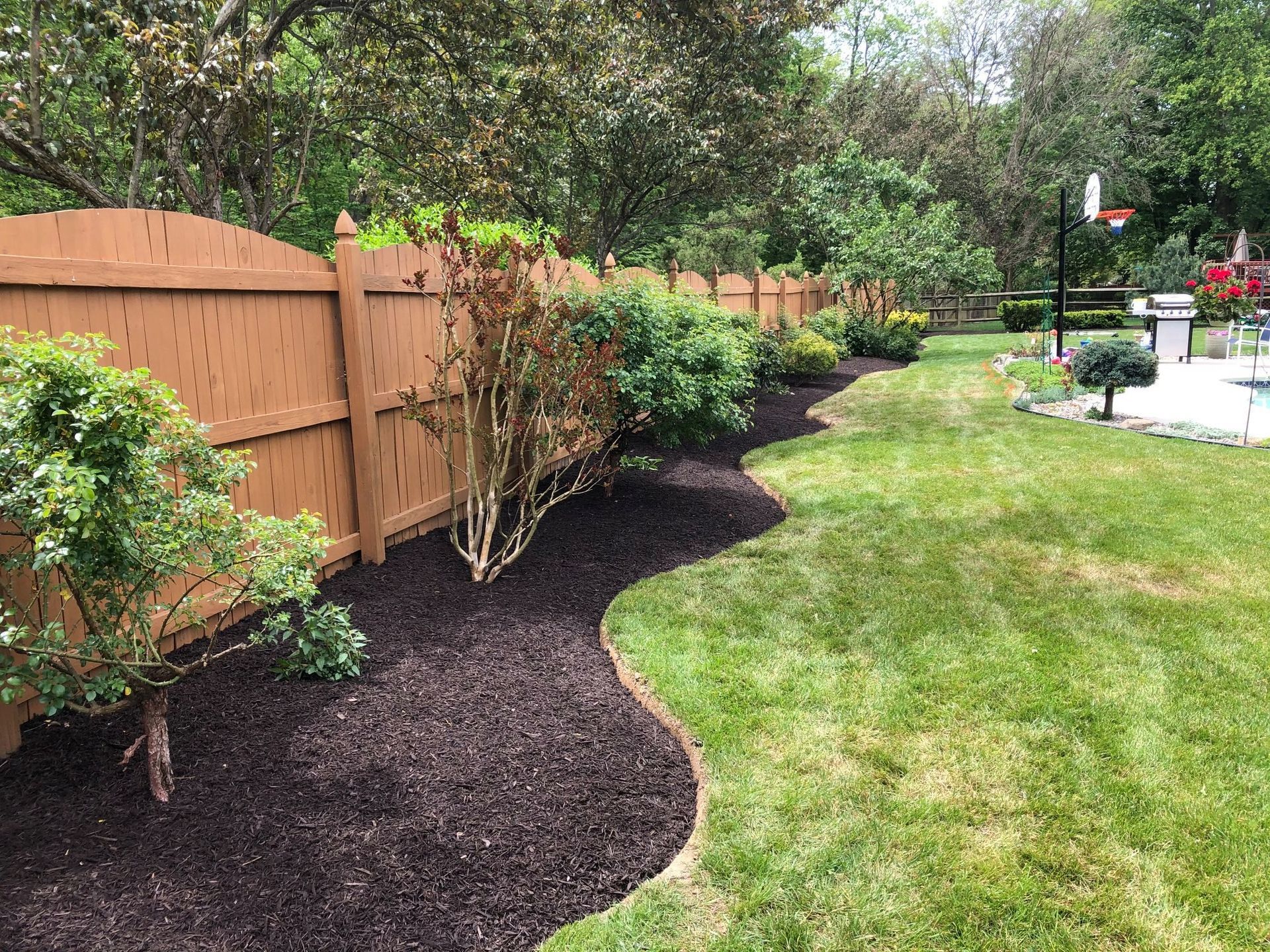 A wooden fence surrounds a lush green lawn in a backyard.
