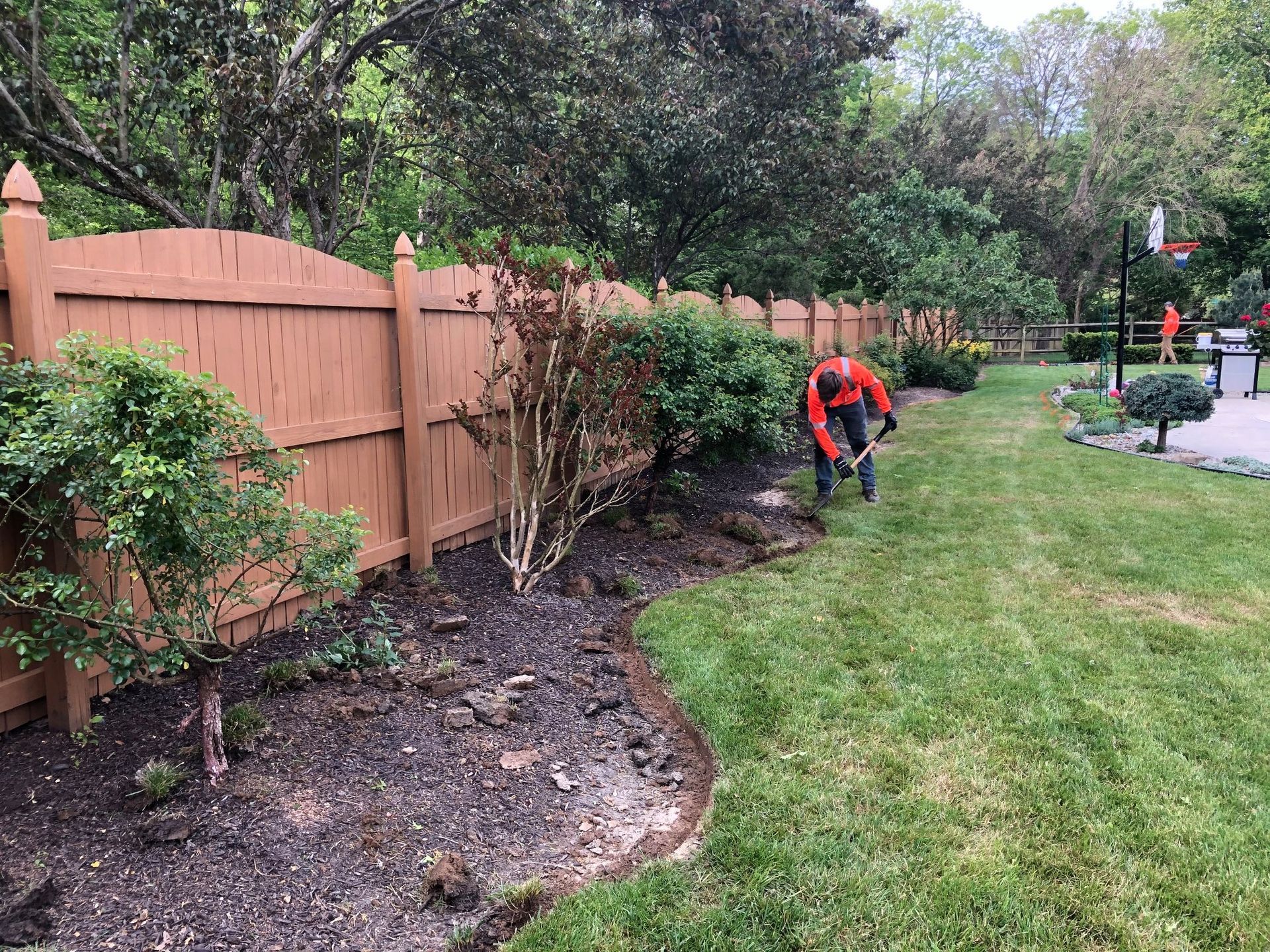 A man is working in a yard next to a wooden fence.