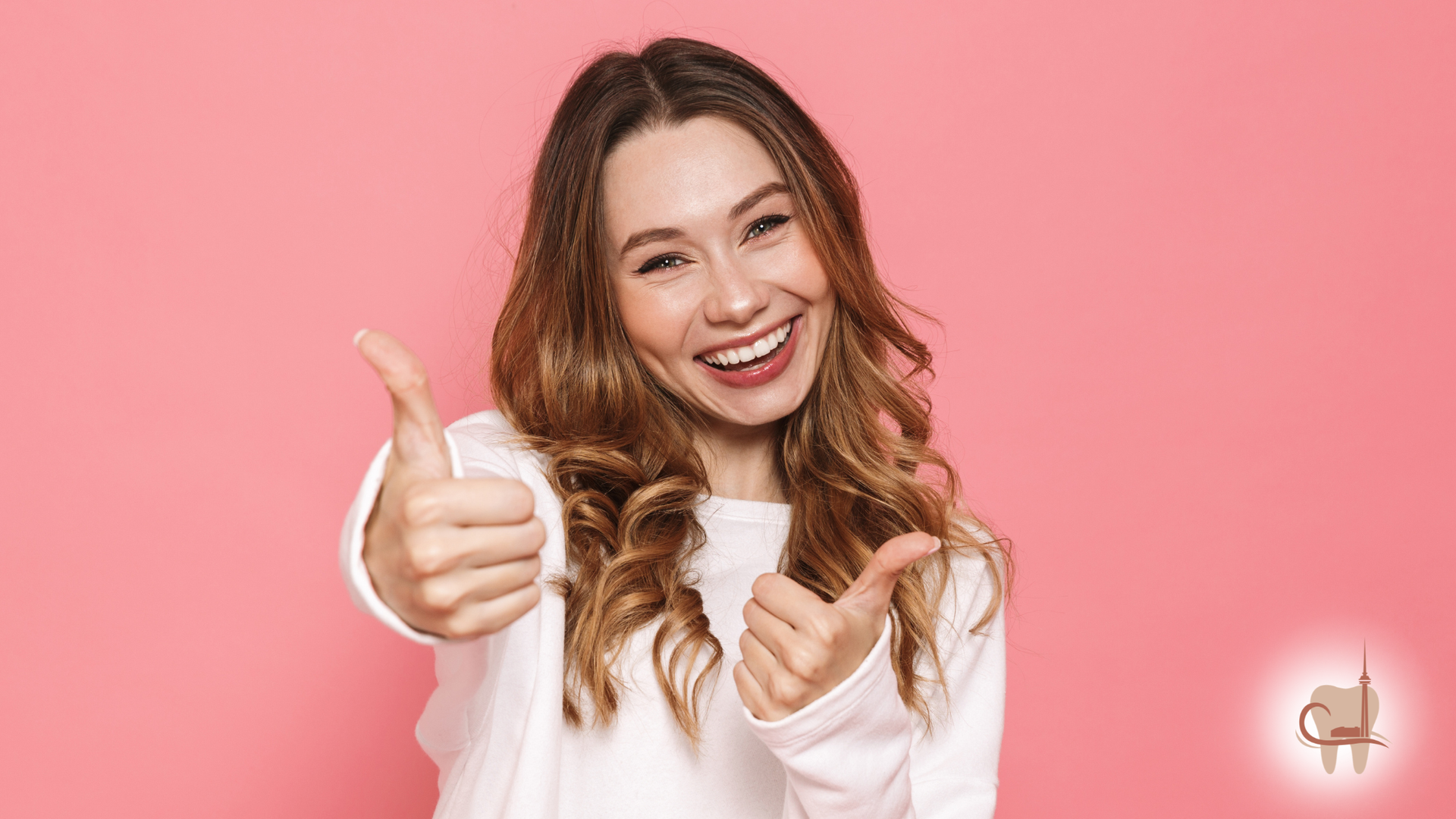 Smiling woman in white sweater giving two thumbs up against a pink background