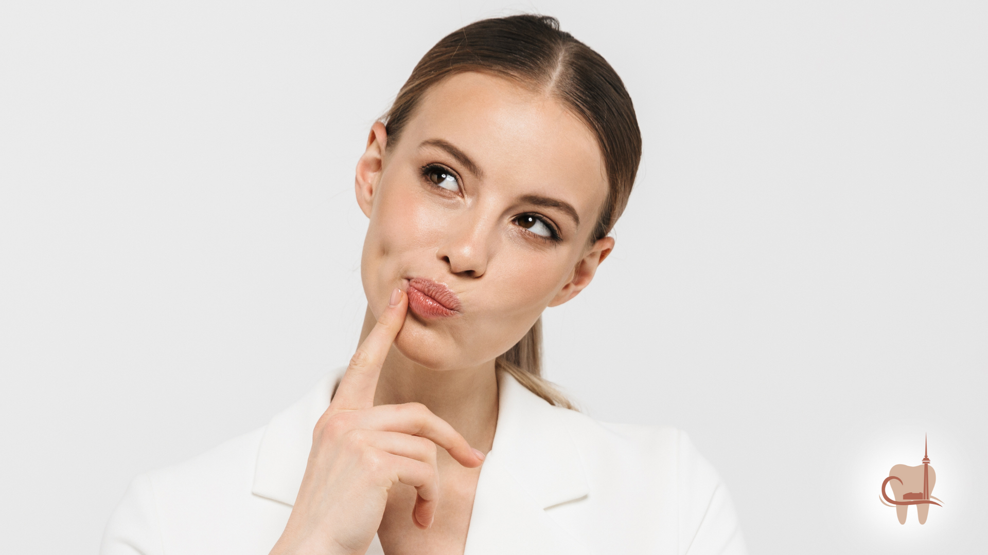 Woman in white blazer, finger on lips, looking up thoughtfully, studio setting.