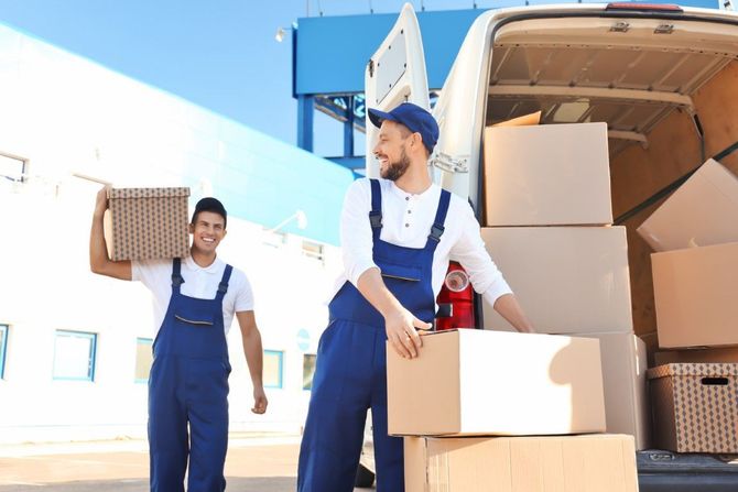 Two movers loading cardboard boxes into a delivery truck outdoors