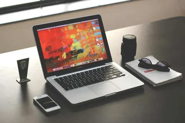 A laptop is open on a desk next to a cell phone and a notebook