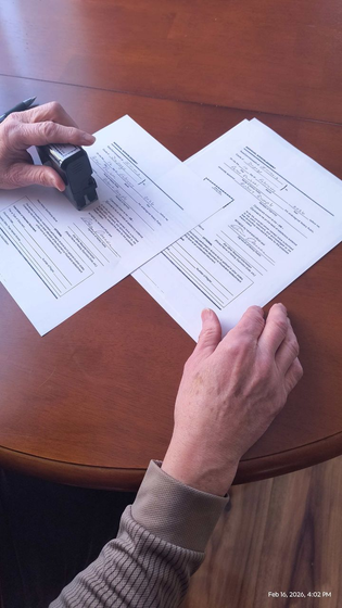Hands reviewing printed documents on a wooden table with a black stamp or stapler.