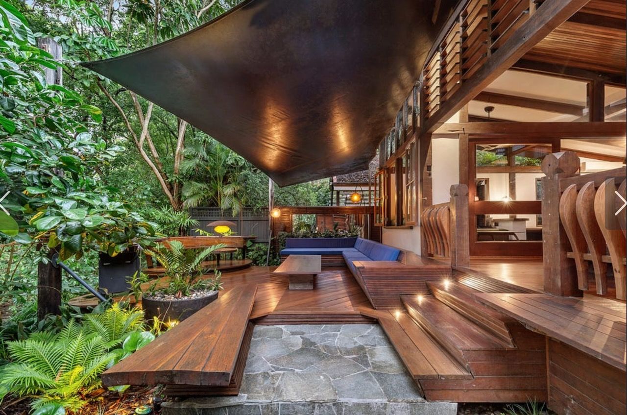Wooden deck with shade sail, leading to an open-air seating area with greenery.