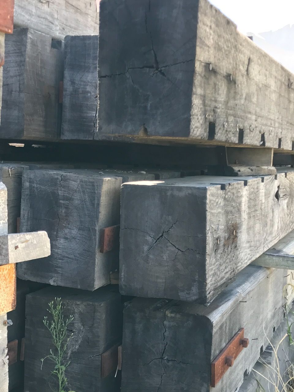 Pile of weathered, dark wooden beams with visible cracks and metal plates in Brisbane.