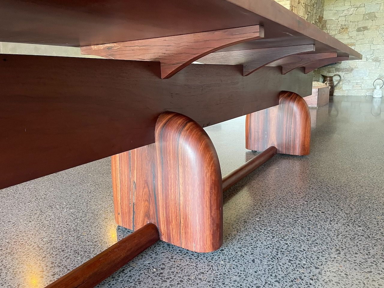 Low-angle view of a large, dark wood table with curved legs and support beams, on a gray stone floor in Brisbane.