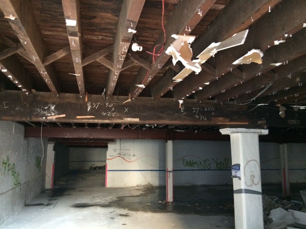 A dilapidated concrete interior with exposed wooden beams and graffiti in Brisbane.