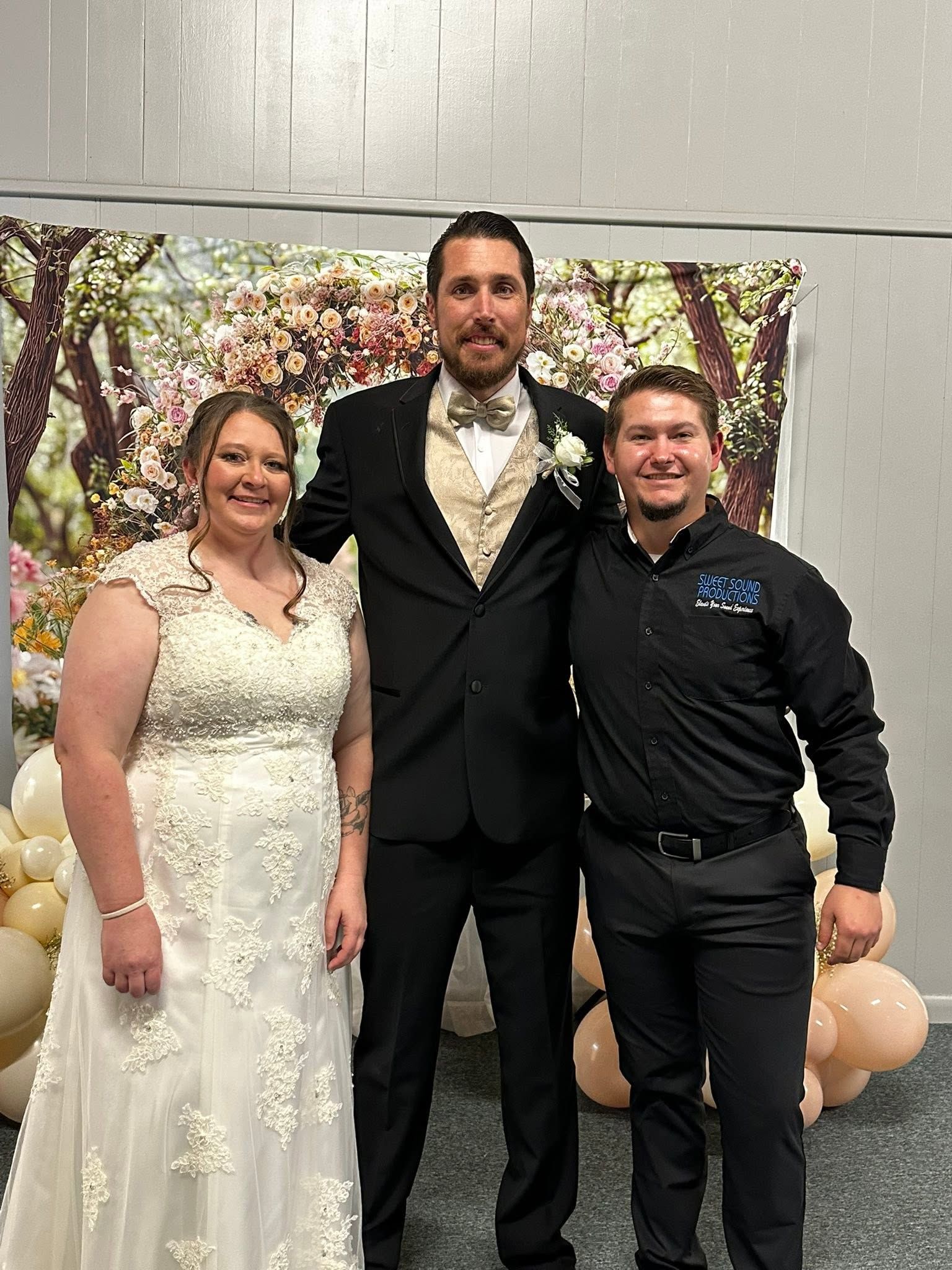 Eric Perdue and wedding couple taking a picture together with floral decor and a balloon backdrop.