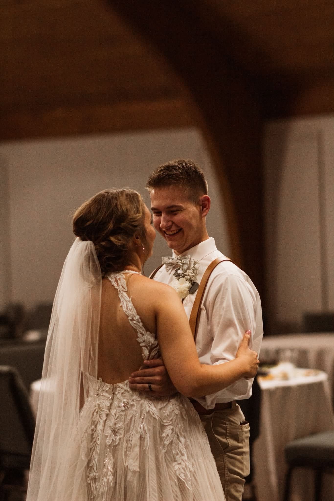 Bride and groom dancing at a wedding reception, smiling in a warmly lit hall