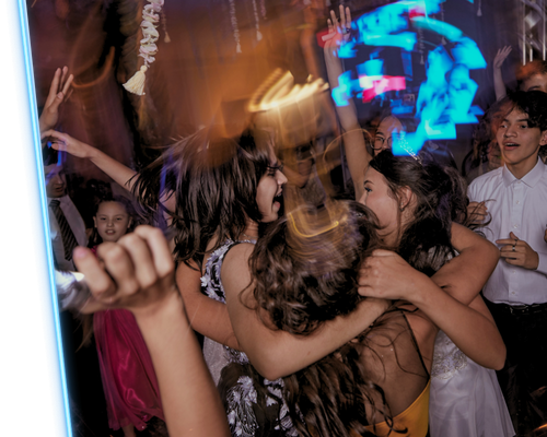 Crowd dancing at a party, with raised hands and colorful neon lights