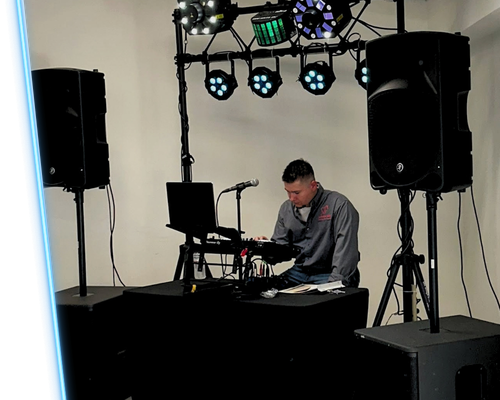 DJ mixing at a table with speakers and stage lights in a simple indoor setup
