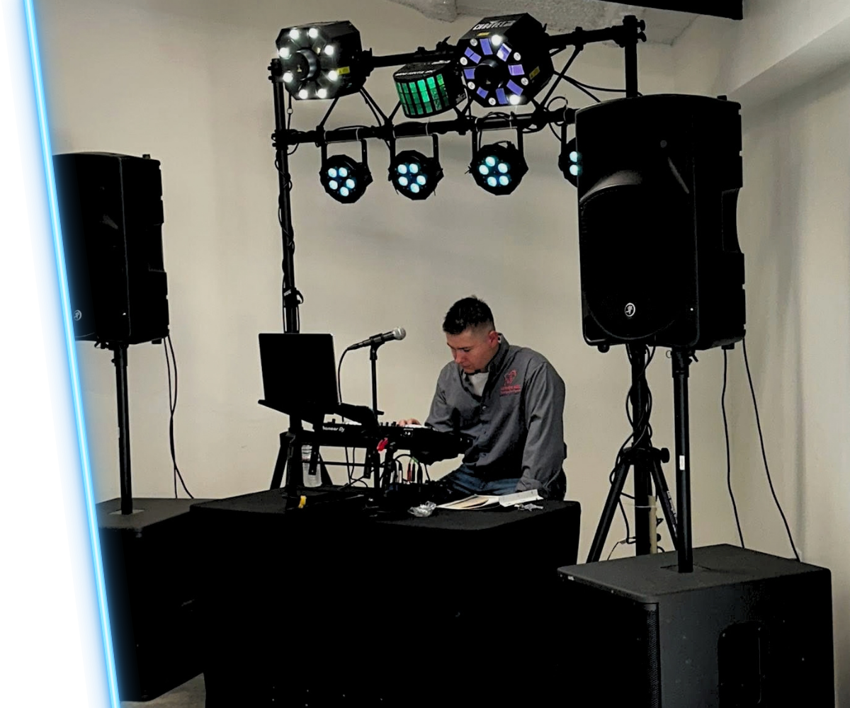 DJ performing at a small indoor setup with speakers, lights, and a laptop on a table