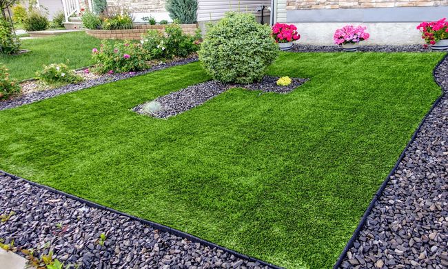 Manicured green lawn bordered by purple gravel and flower beds in a landscaped garden Manicured green lawn bordered by purple gravel and flower beds in a landscaped garden
