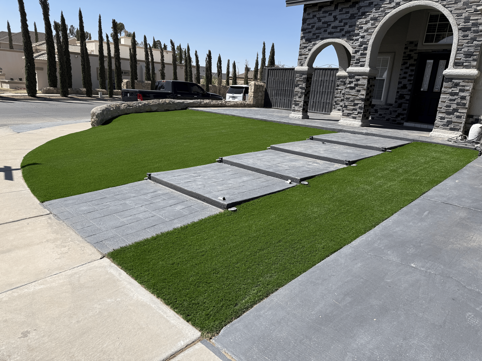 Stone walkway and stepping stones across a green lawn leading to a stone house entrance