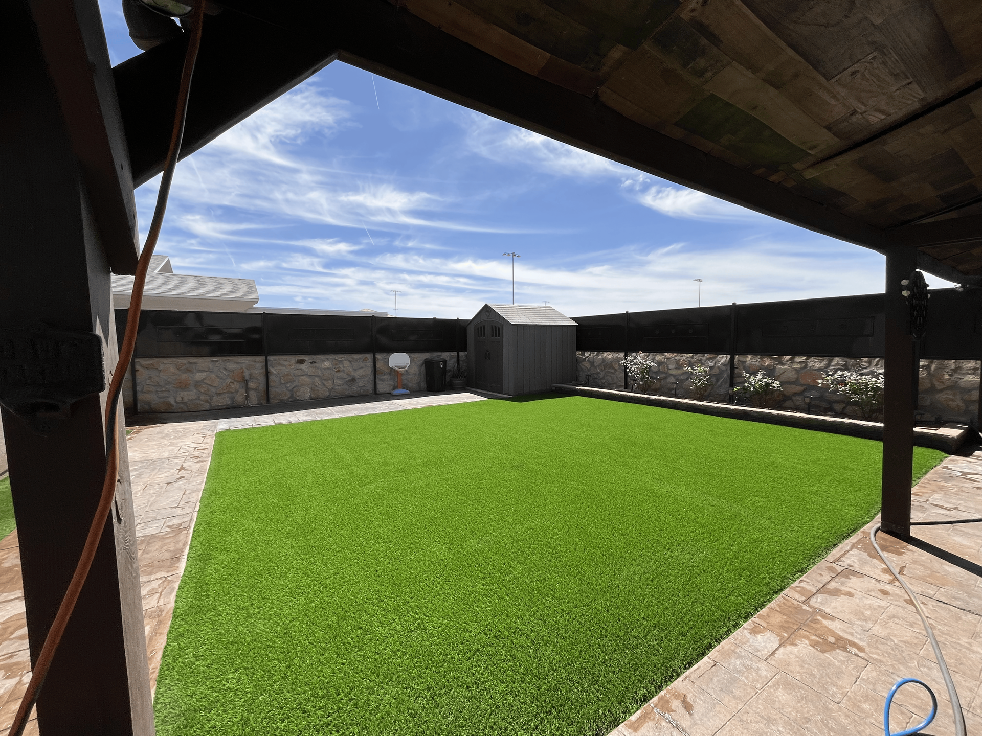 Covered patio with bright green artificial turf and fenced yard under a blue sky