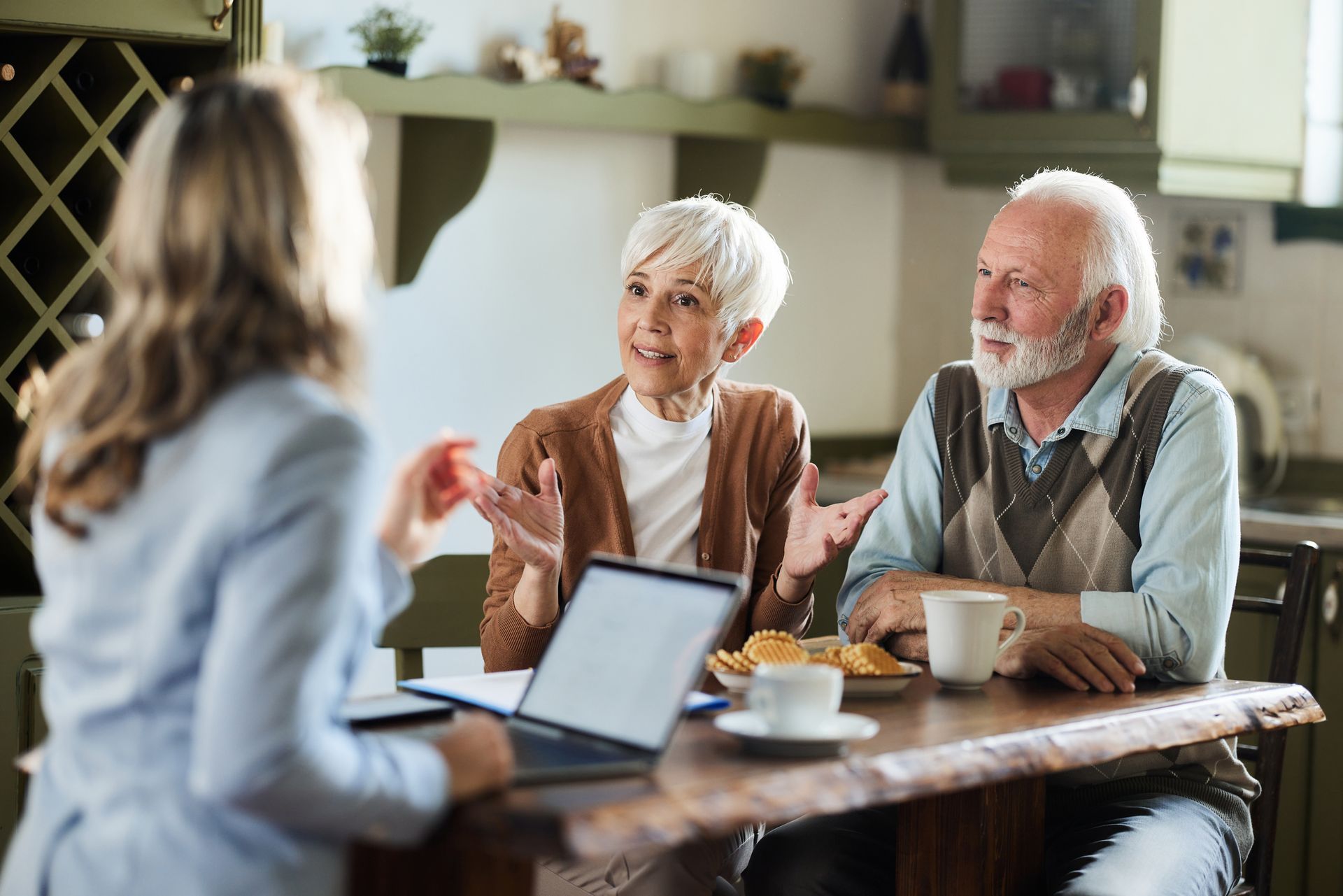 An elderly couple is sitting at a table talking to a woman.
