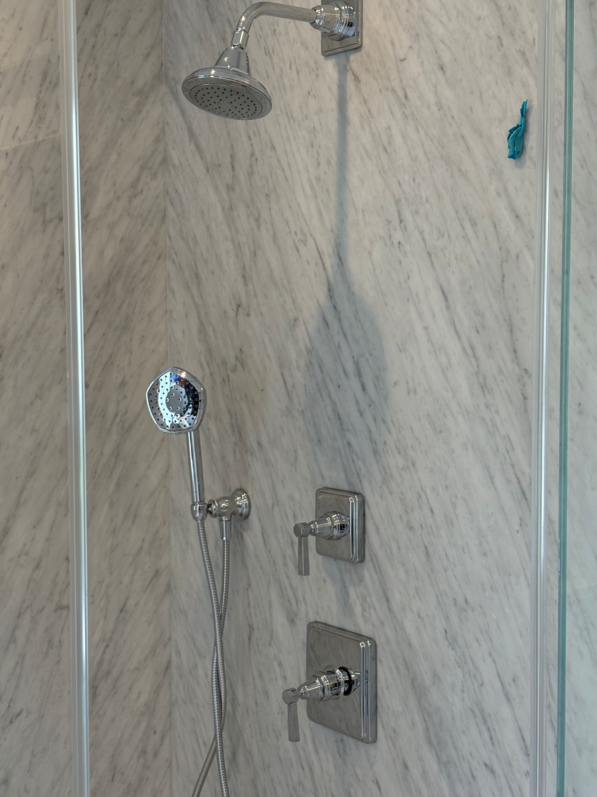 Shower stall with chrome showerhead, handheld sprayer, and control valves on beige tiled wall