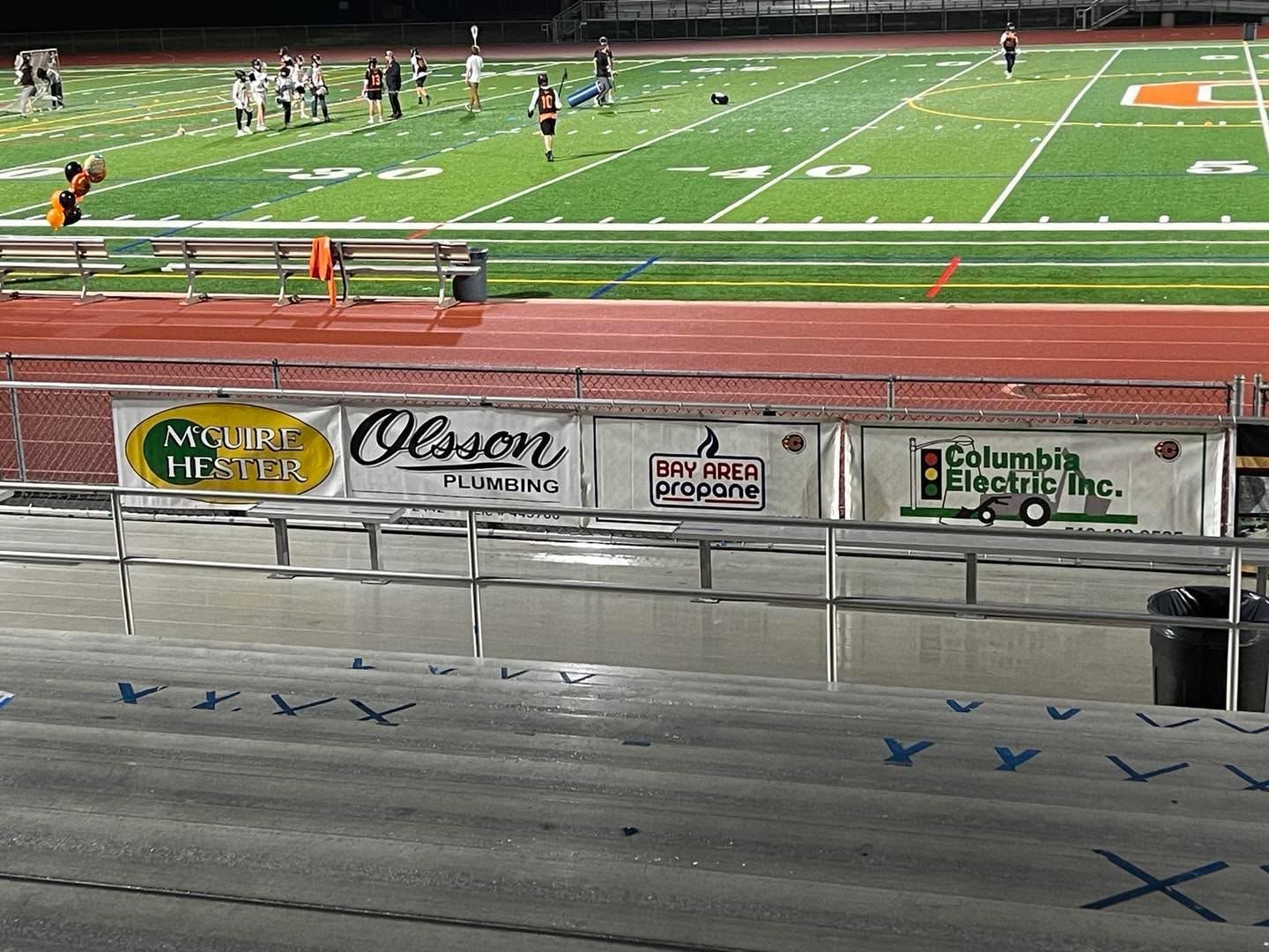 Empty bleachers beside a football field with players in the distance at night