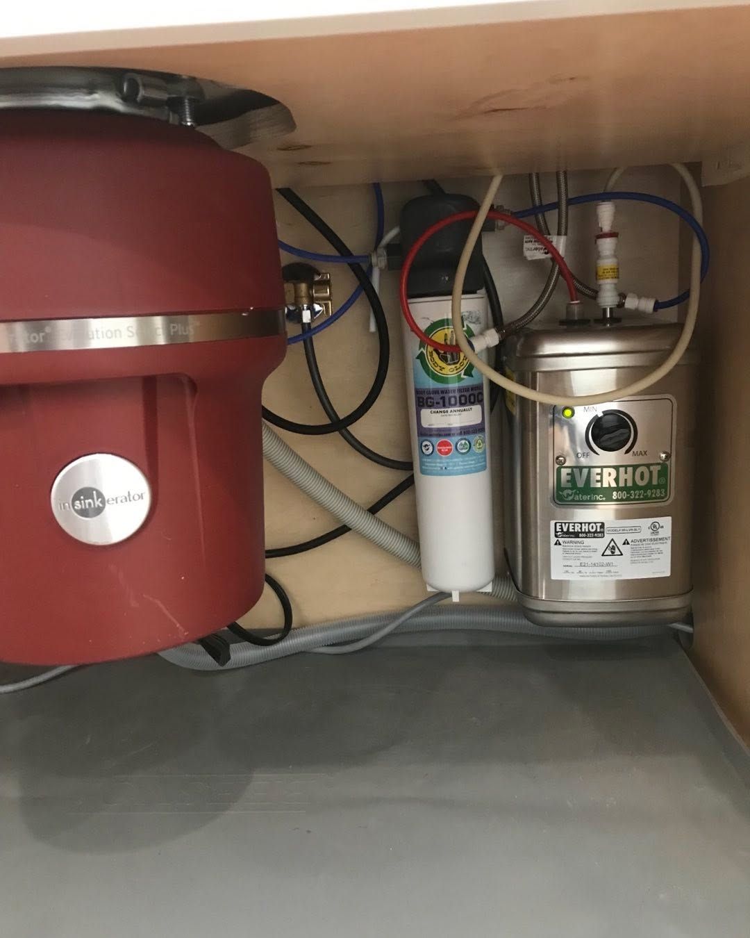 Under-sink plumbing with pipes, a garbage disposal, water filter, and a hot water tank