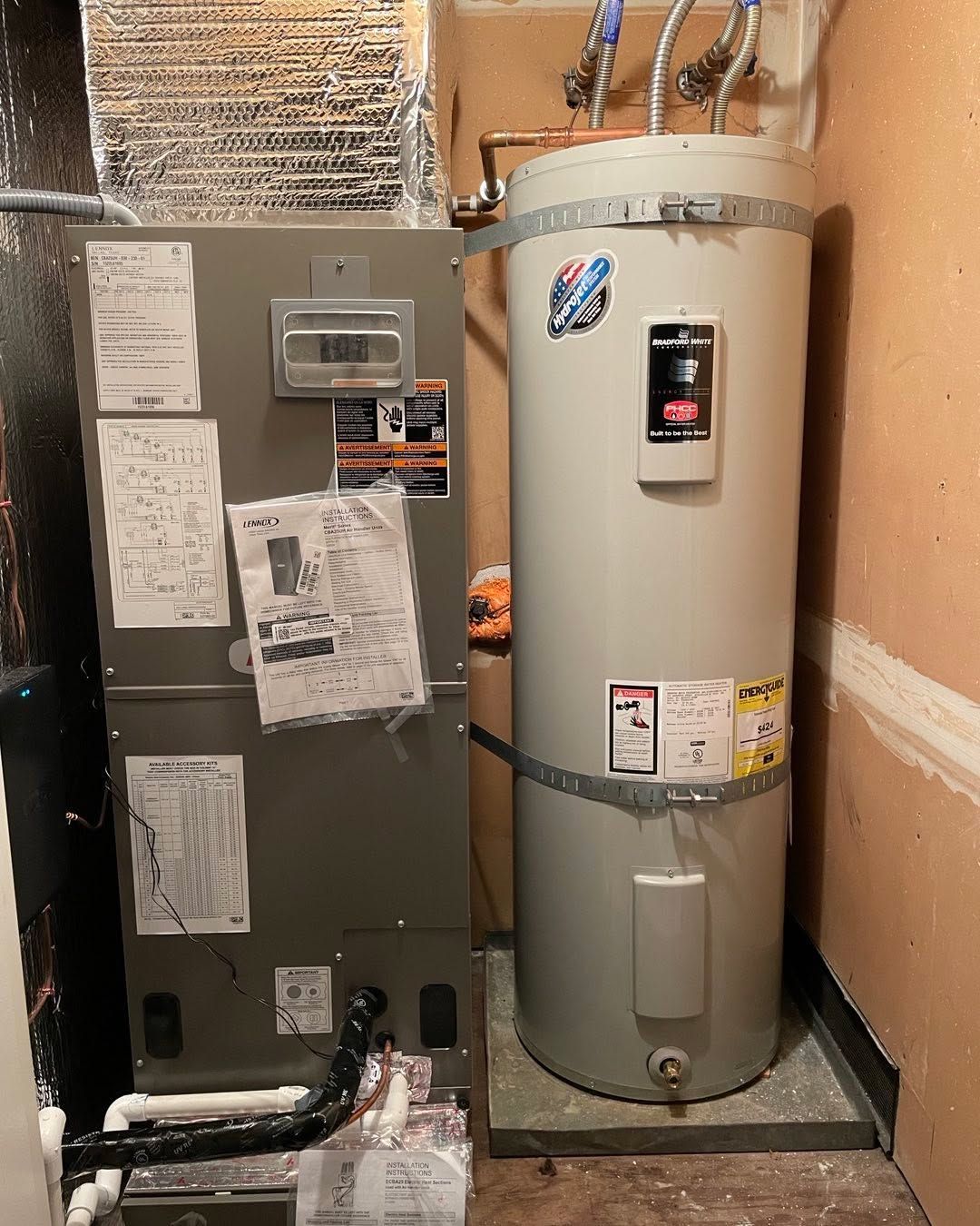Water heater beside a gray HVAC unit in a small utility closet with exposed ductwork and pipes.