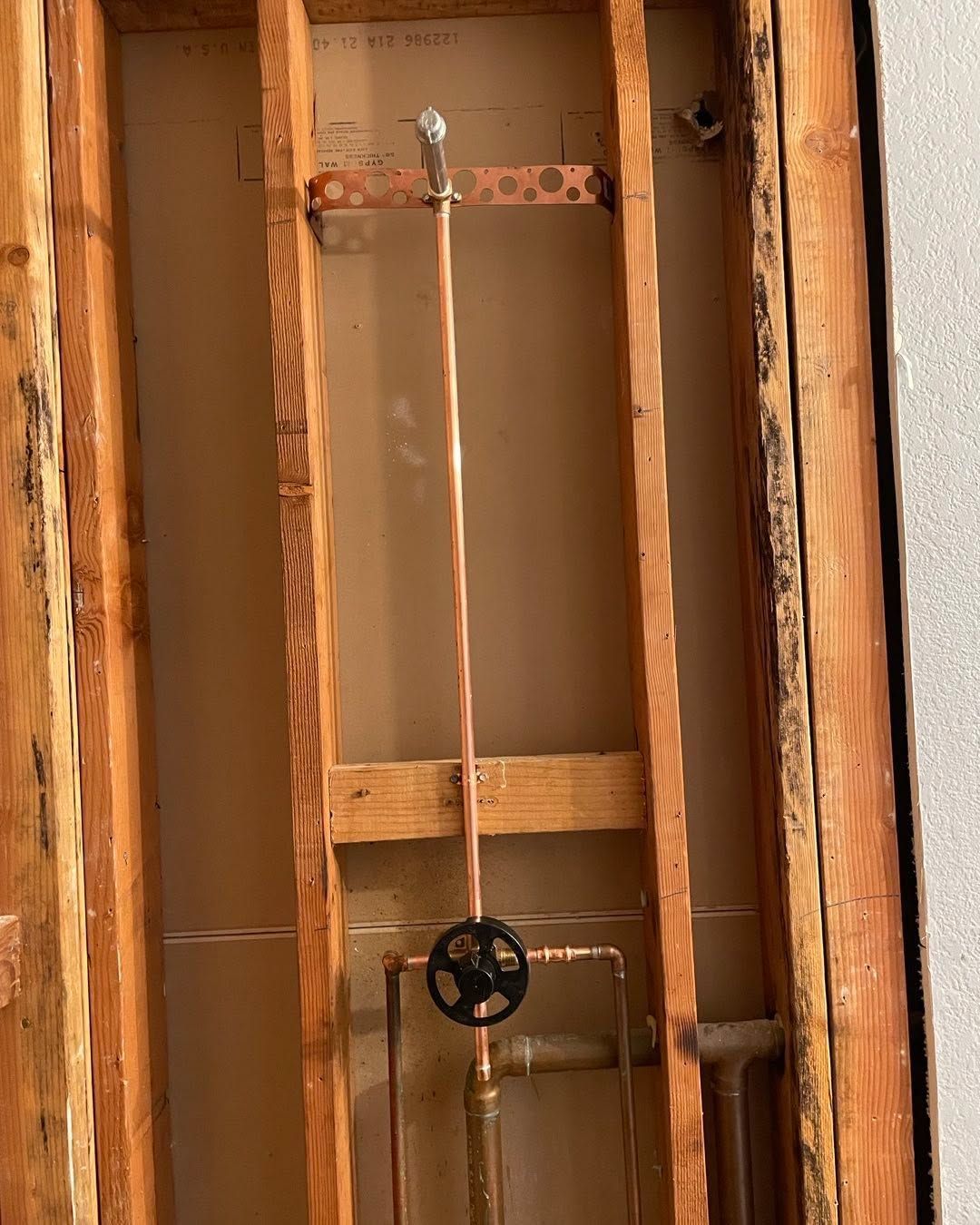 Open wall framing with exposed pipes and a black valve handle in a construction area