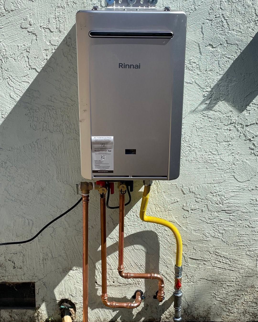 Rinnai tankless water heater mounted on a stucco wall with exposed copper and yellow gas piping