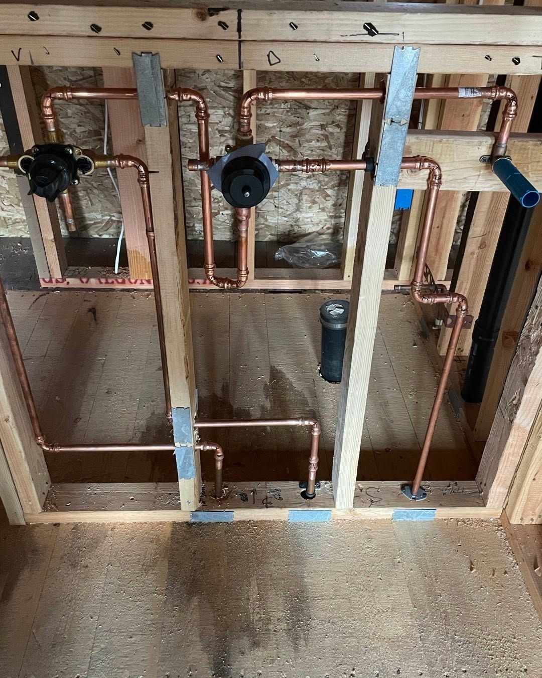Exposed plumbing pipes and wall framing in an unfinished room with concrete floor and insulation.