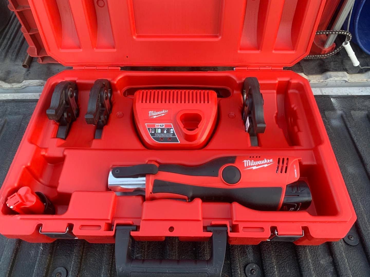 Red tool case with a cordless drill, charger, batteries, and accessories arranged inside.