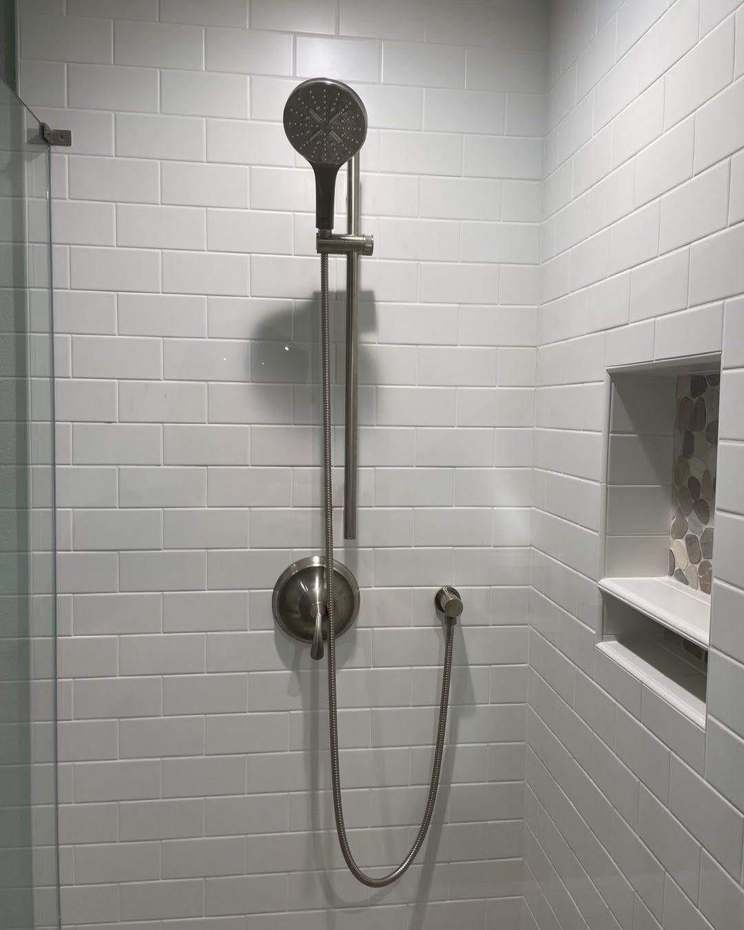 White tiled shower with handheld and overhead showerheads and built-in wall niche.