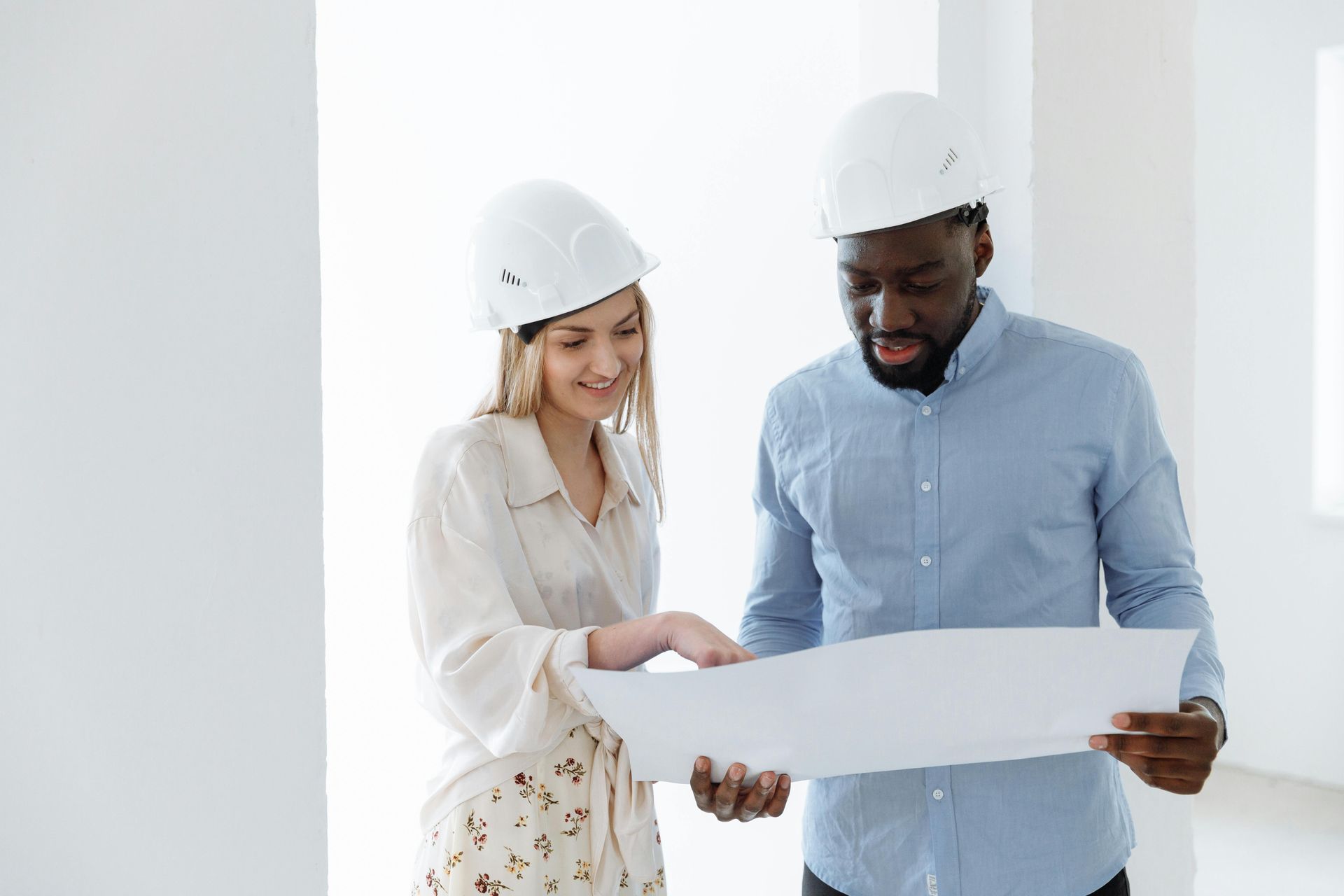 Two people in hard hats looking at a blueprint in a white room.
