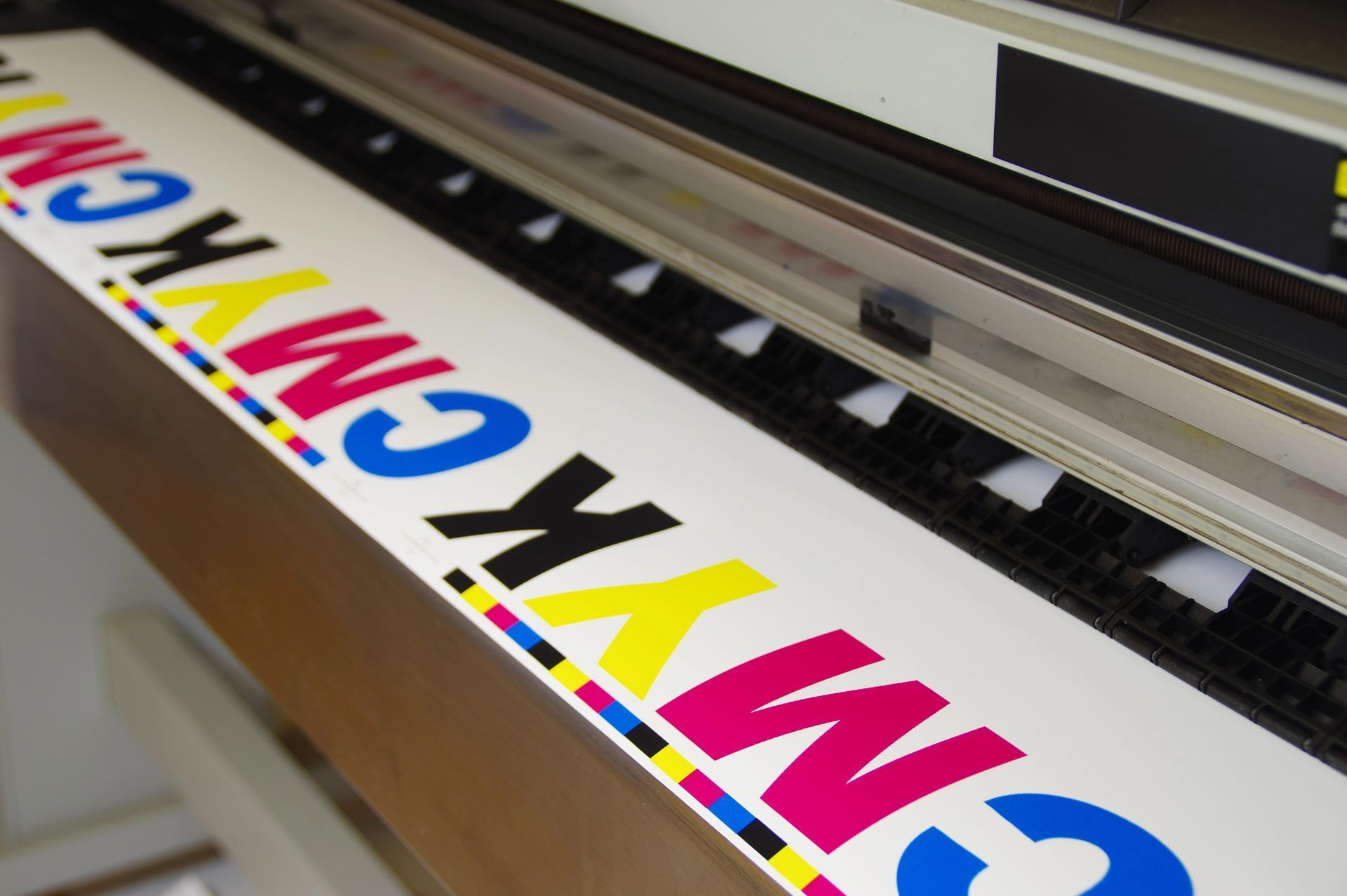 Impresora de gran formato imprimiendo letras de colores en CMYK sobre una pancarta blanca