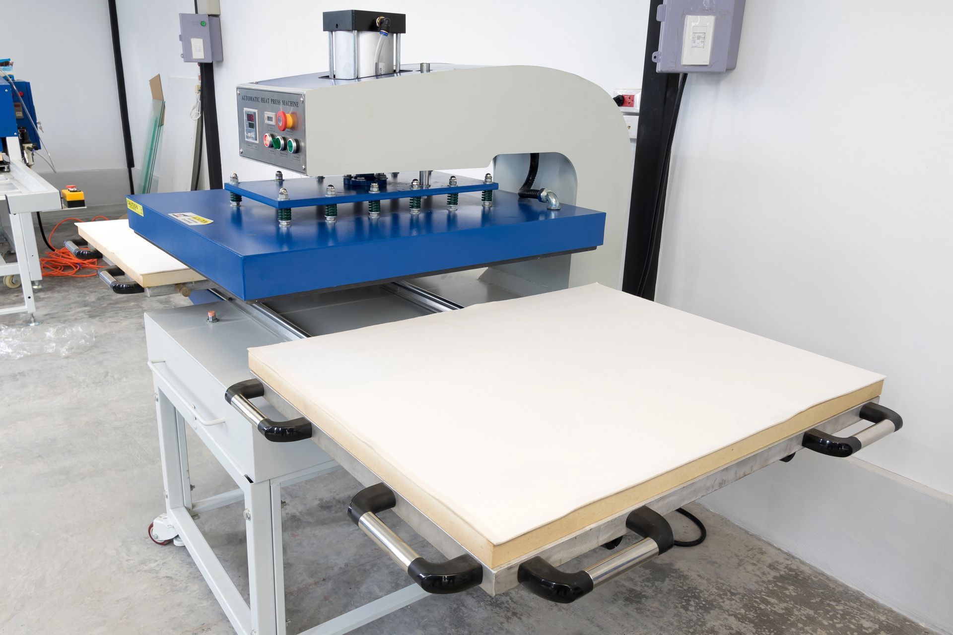 Prensa industrial con estructura metálica azul y una gran mesa de trabajo blanca en un taller