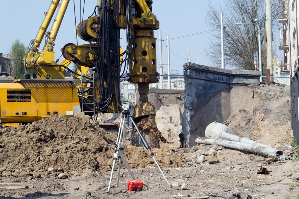 A Yellow Excavator With a Level on a Tripod — North Coast Drilling & Wicks in Bangalow, NSW