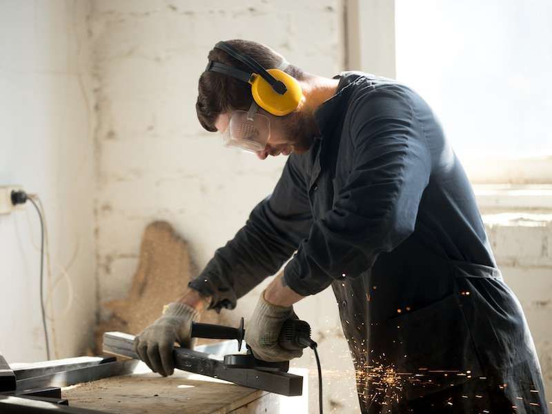 Person in yellow earmuffs using a grinder on metal, with sparks flying in a workshop.