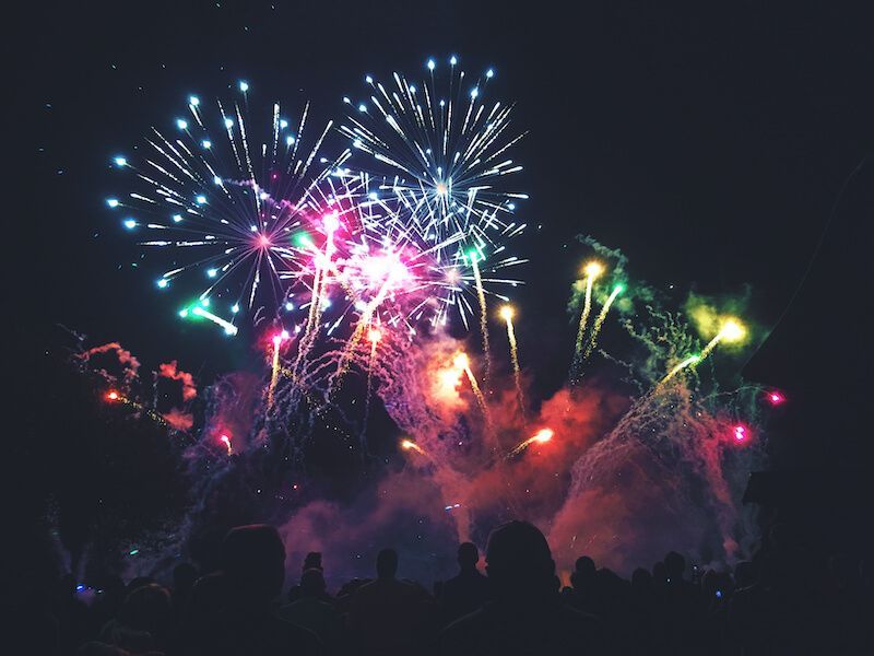 Colorful fireworks bursting in the night sky above a crowd silhouette