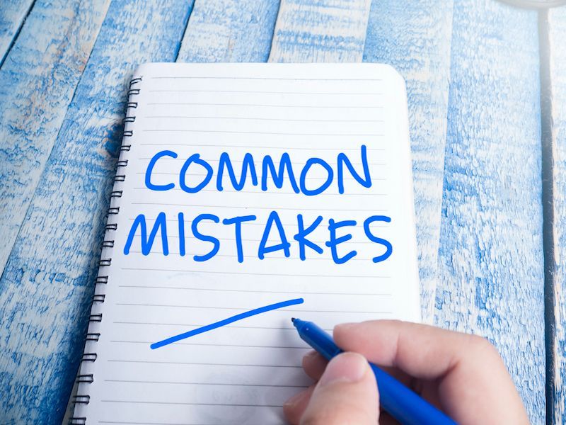 Notebook page reading “COMMON MISTAKES” with a hand holding a blue pen on a blue wooden surface