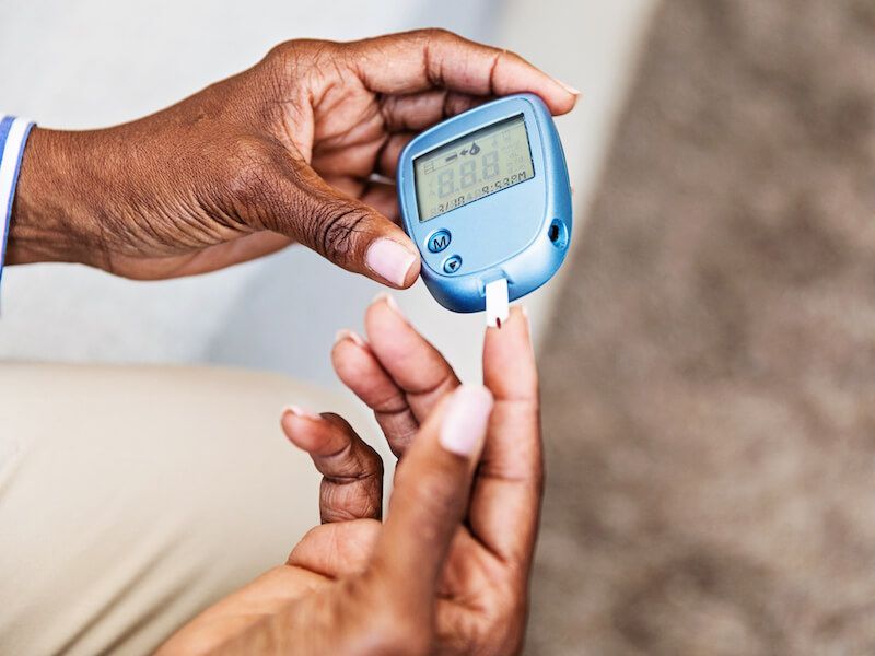 A hand uses a blood glucose meter to test a fingertip