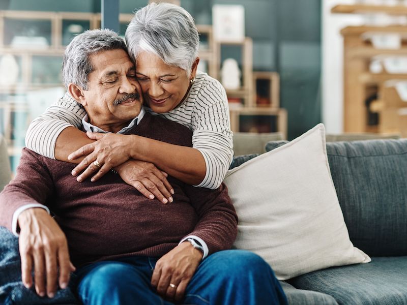 Two people embracing on a couch in a cozy living room, smiling warmly