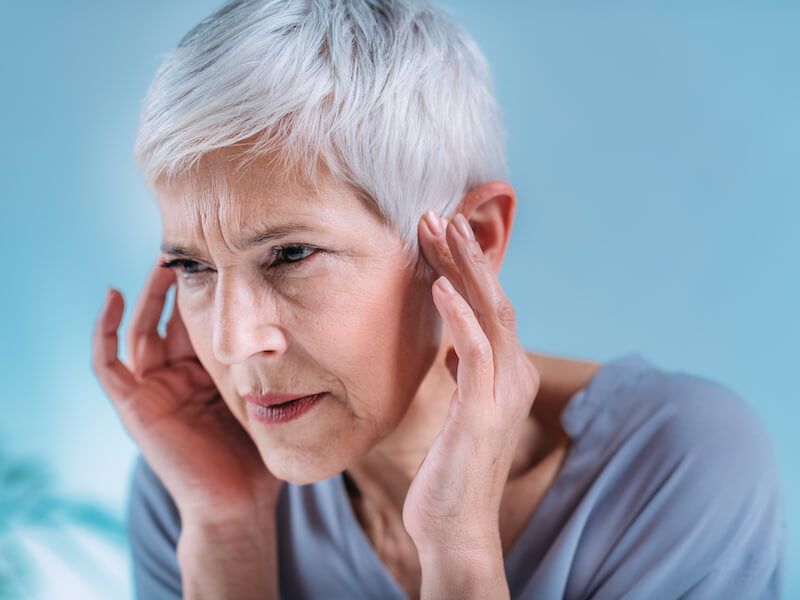 Woman with short white hair holding her head and looking pained against a blue background