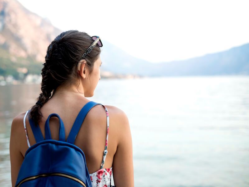 Person with blue backpack looking over a bright lake with mountains in the background