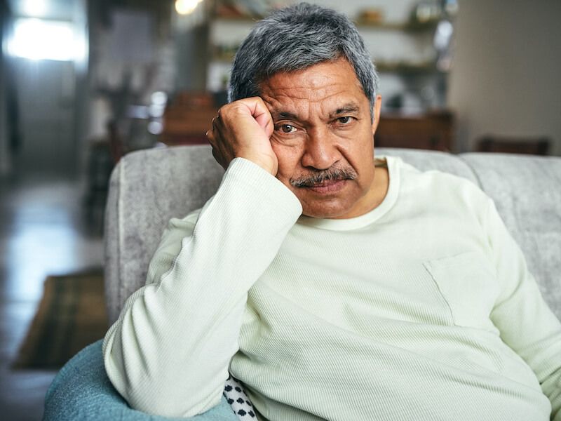 Man sitting on a sofa, resting his head on his hand with a pensive expression.