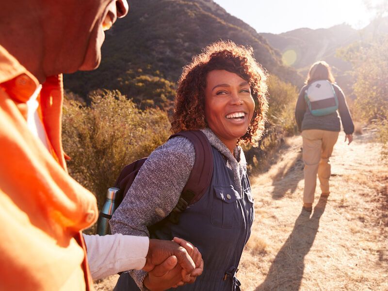 Two hikers holding hands on a sunny trail, smiling as they walk uphill together