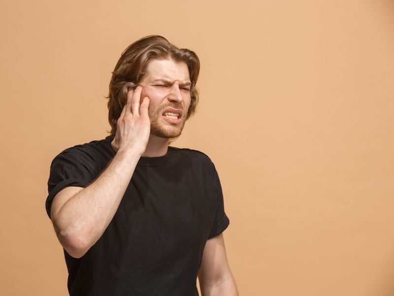 Man in black shirt rubbing his face against a beige background