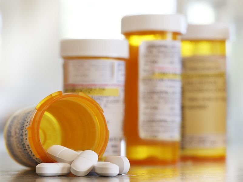 Prescription pill bottles with orange lids and white tablets spilled in front of them