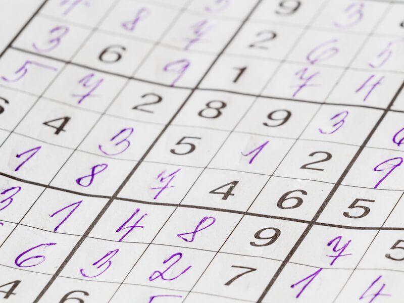 Close-up of a Sudoku puzzle grid with printed black numbers and purple handwritten notes on white paper