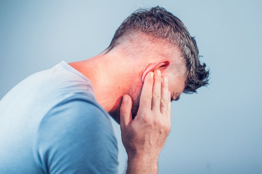 Man holding his head in pain, with a red glow around his ear against a blue background