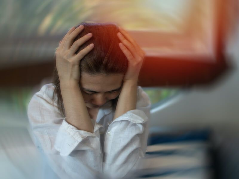 Person sitting with head in hands, appearing stressed or overwhelmed indoors