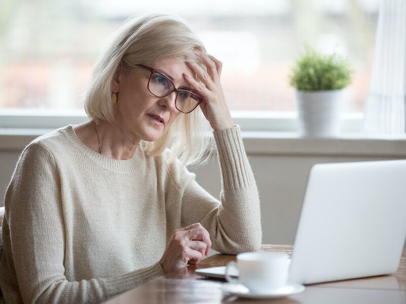 Woman sitting at a desk, holding her head while looking at a laptop and coffee cup