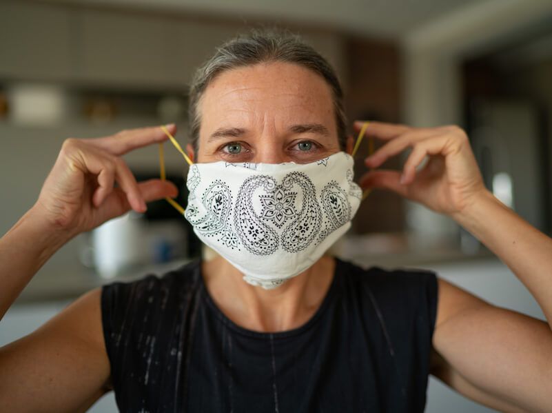 Person adjusting a white patterned face mask indoors, with a blurred home background.